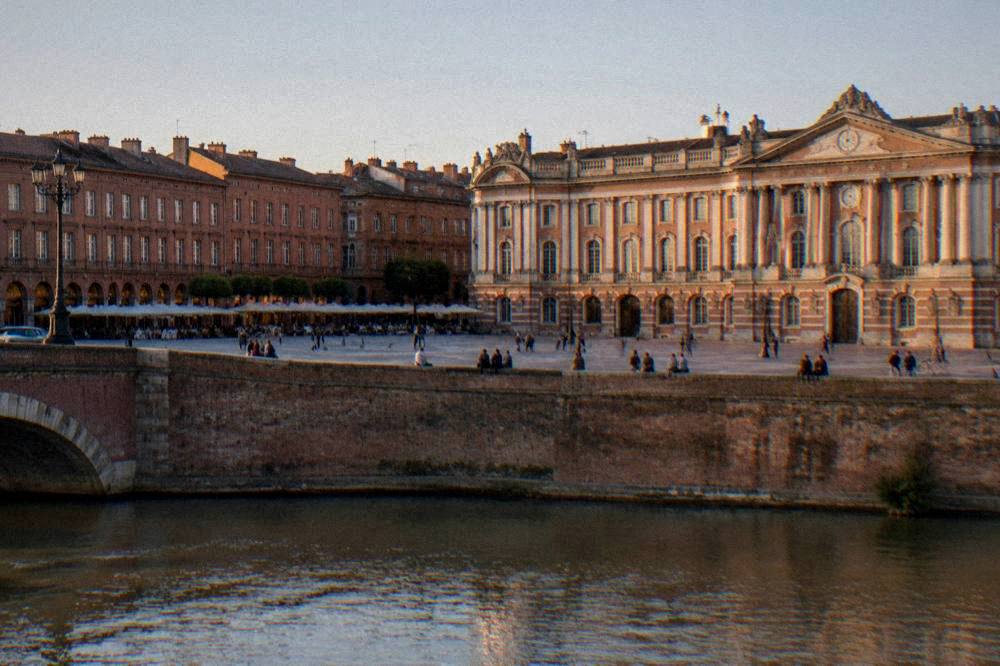 A sunlit city square with pink-toned brick buildings and outdoor tables