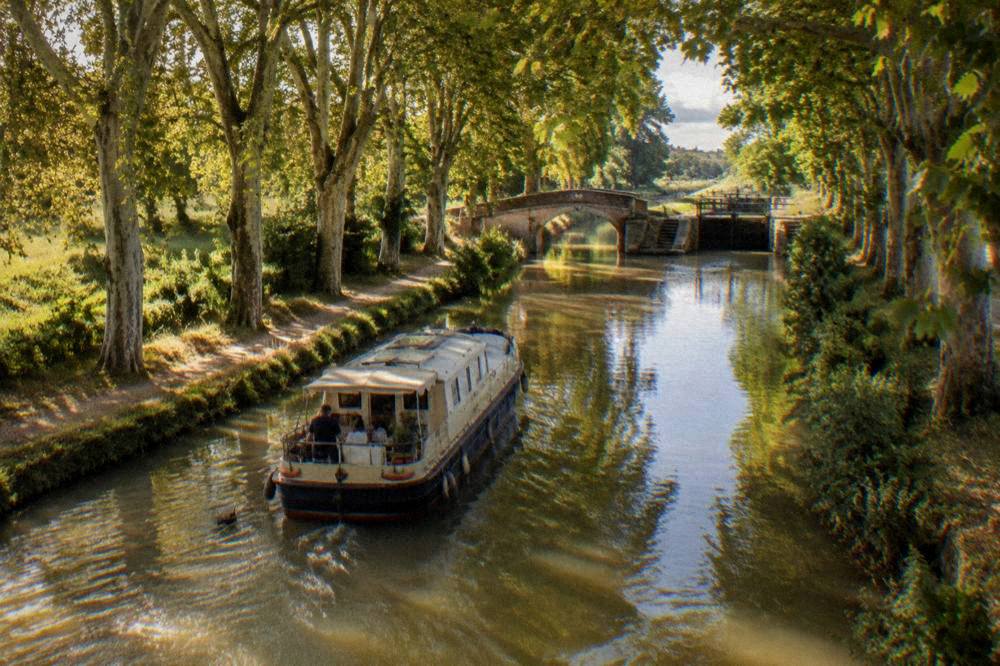 A canal boat gliding under plane trees on the Canal du Midi in late afternoon light
