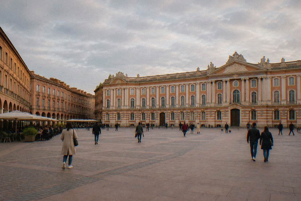 Wide flat plaza in front of the pink brick Capitole building in Toulouse with people strolling