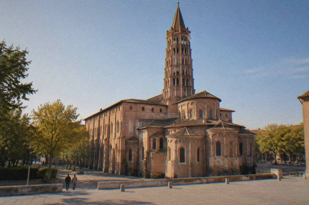 Basilica of Saint-Sernin in Toulouse seen from a level stone square with a smooth paved foreground