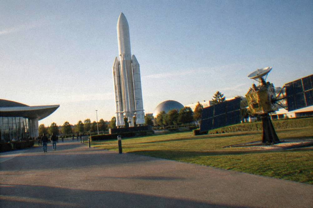 Rocket and satellite exhibits standing in open outdoor pathways at Cite de l'espace in Toulouse