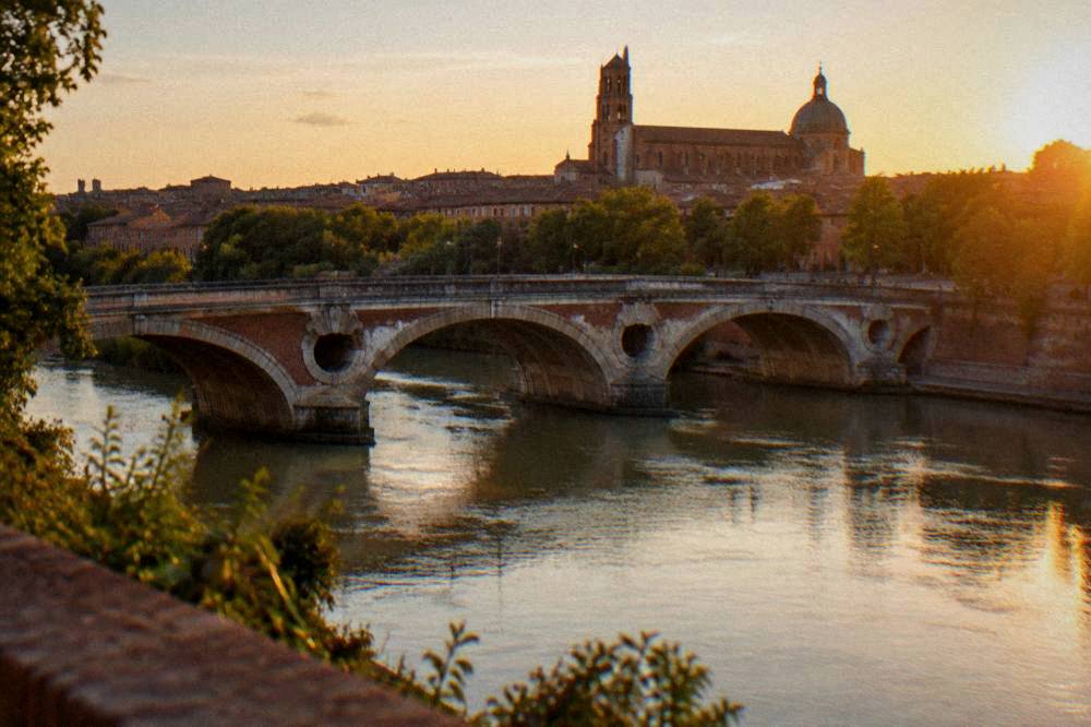 Evening view over Toulouse rooftops with the Garonne river and Pont Neuf bridge in warm light