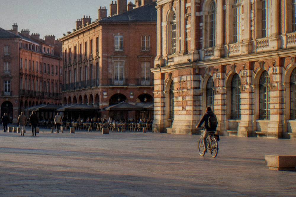 A cyclist riding past pink brick buildings along a Toulouse street