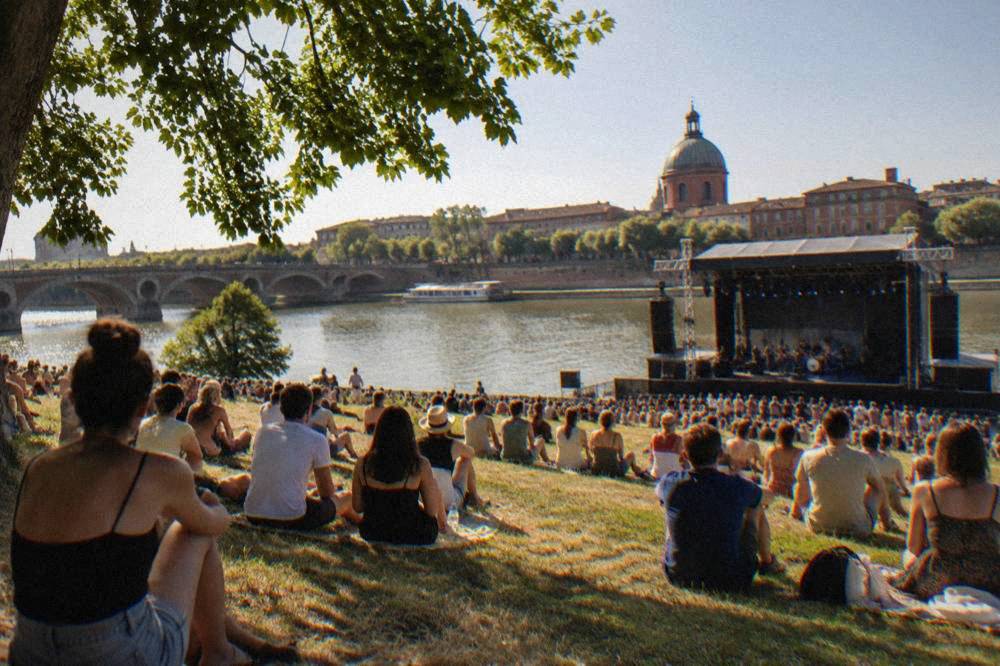 Open-air concert crowd on a riverside meadow in Toulouse in early summer