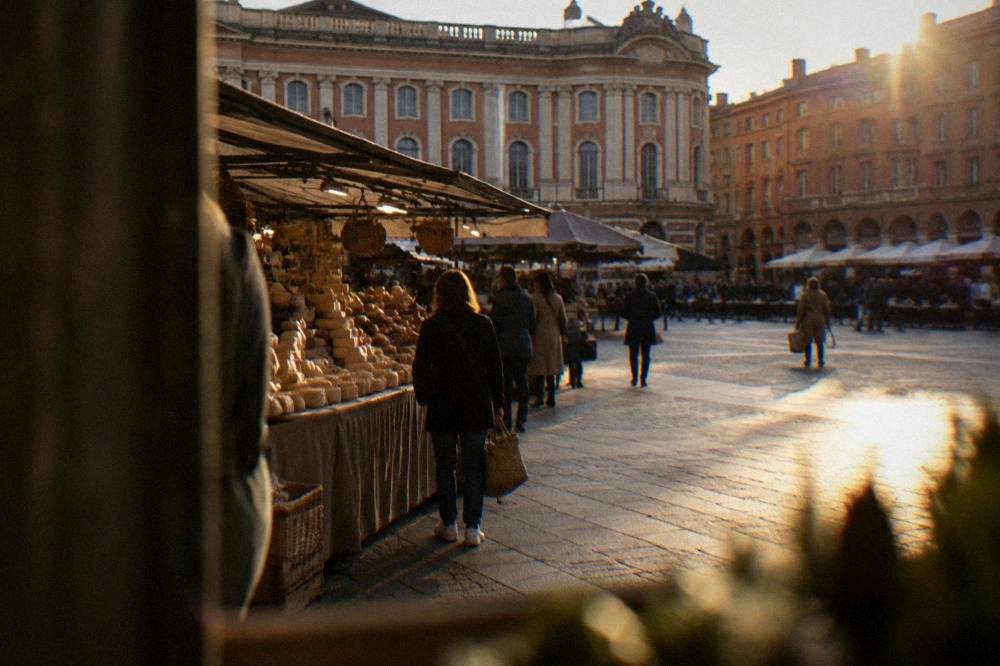 A covered market hall with cheese and charcuterie stalls and shoppers carrying baskets