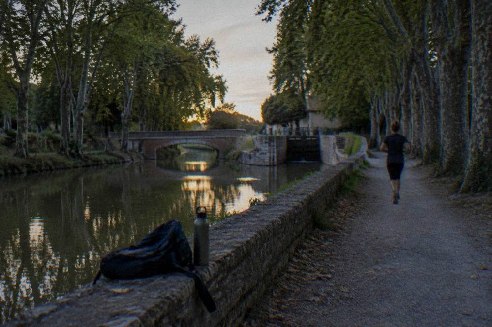 A backpack and water bottle resting on a stone wall beside a canal towpath