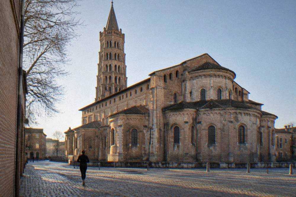 The stone bell tower and Romanesque nave of the Basilique Saint-Sernin in Toulouse under a clear sky