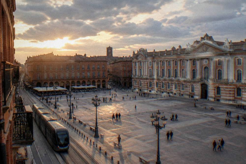 A modern city street in Toulouse with pink brick facades beside a tram line at dusk
