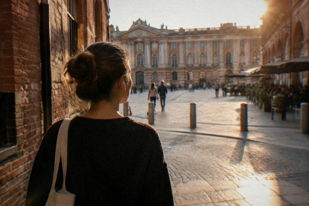 A visitor walking with earphones through a narrow pink brick street in Toulouse
