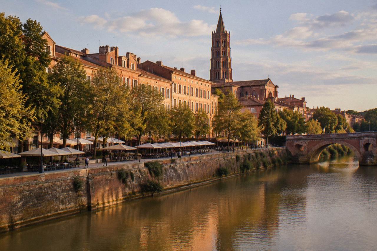 Pink brick buildings along a Toulouse street with the tower of a historic church rising behind them