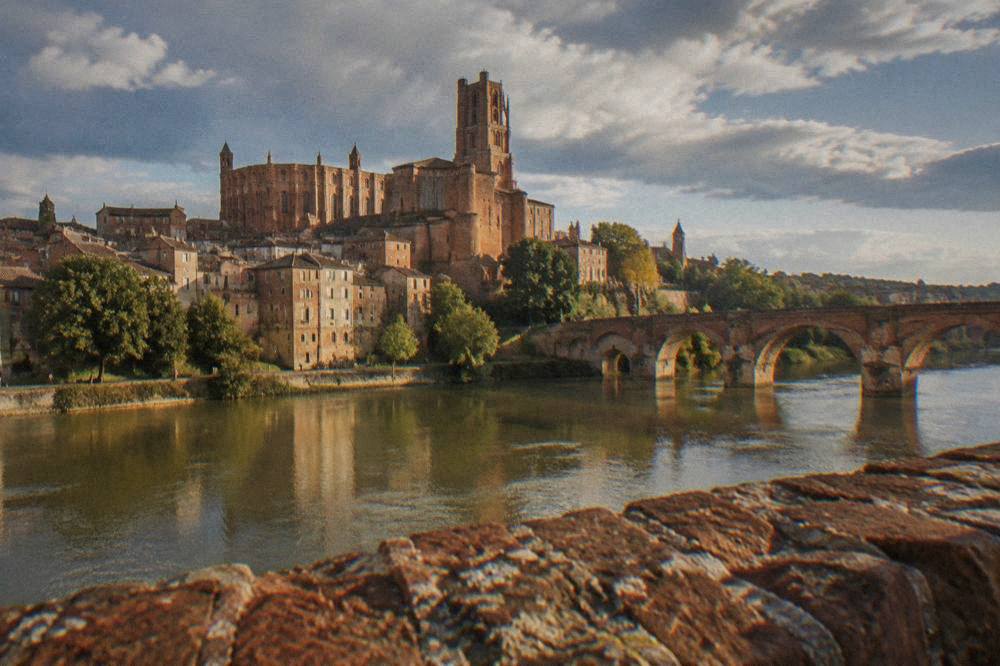 A fortified red brick cathedral beside a river with old stone bridges