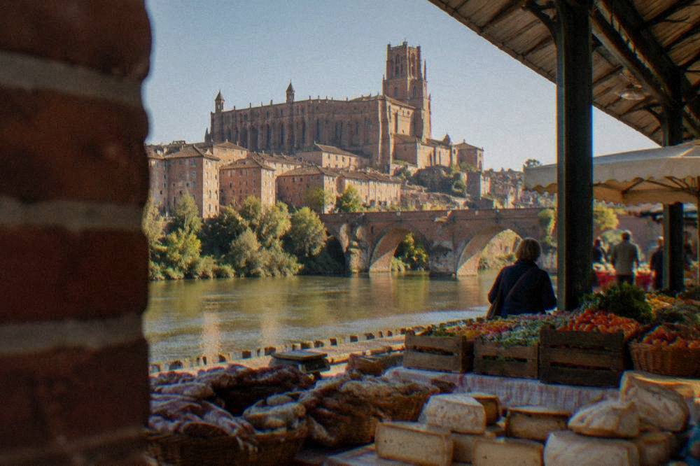 A covered market hall with stalls of cheese, sausage and fresh produce