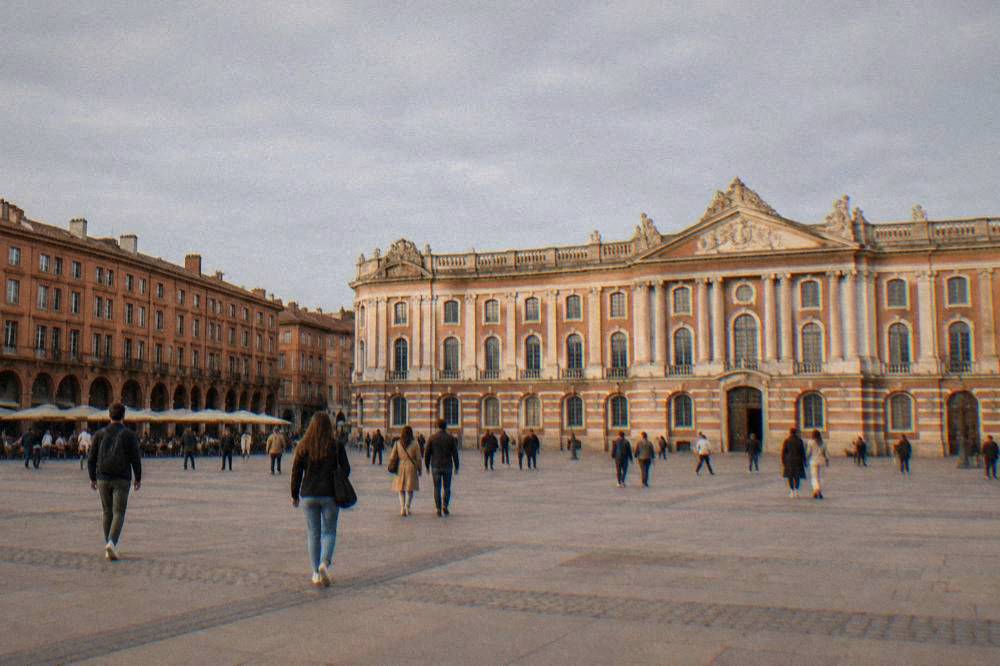 Visitors walking past the pink brick facade of the Capitole in Toulouse