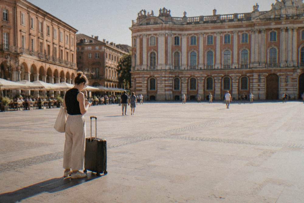 Person checking a phone app next to a suitcase in a city square