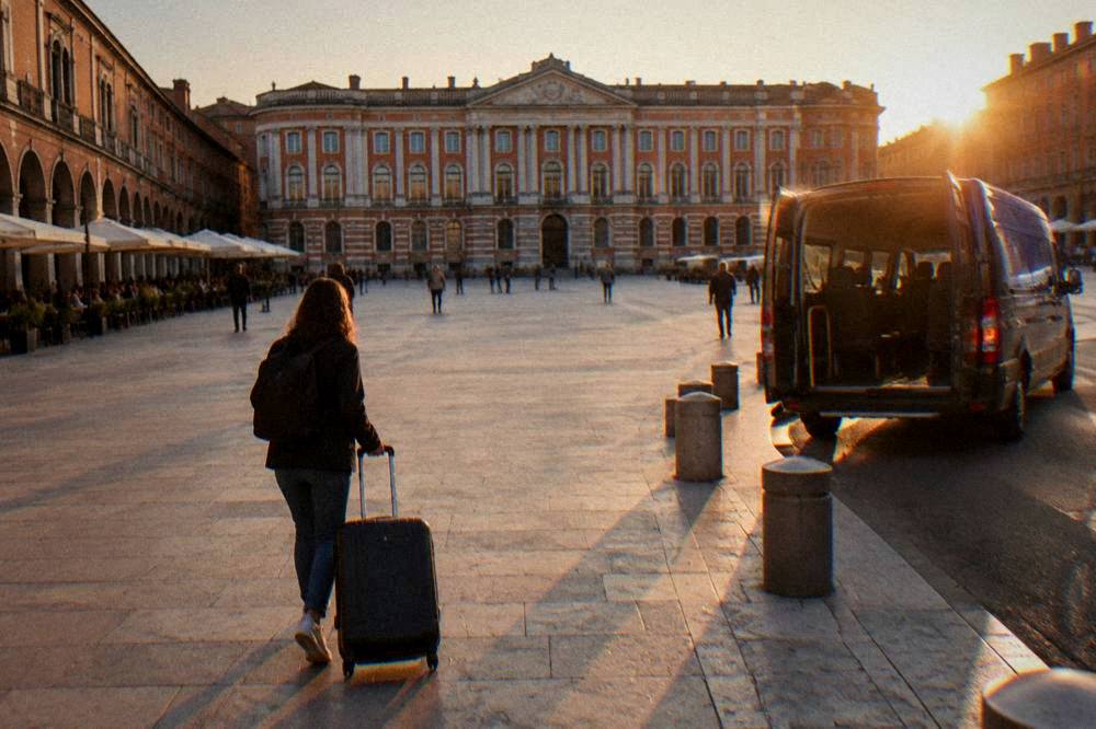 Suitcase being wheeled toward an airport shuttle at dusk in a French city