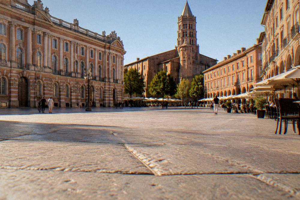 A tall brick basilica with a rounded stone tower seen from a plaza in warm light