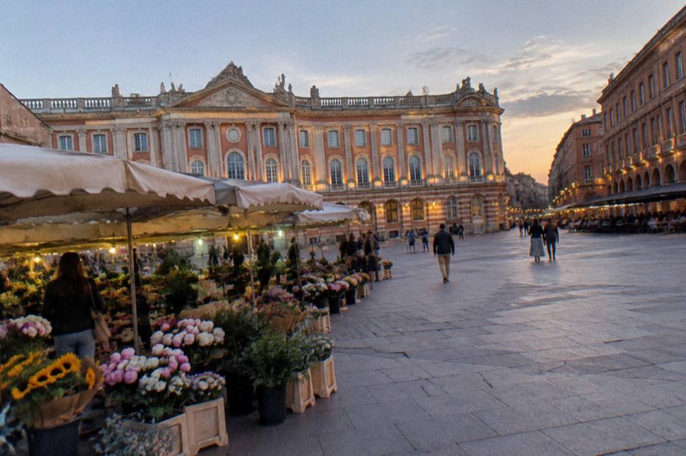 Flower market stalls in front of a pink brick city square in Toulouse