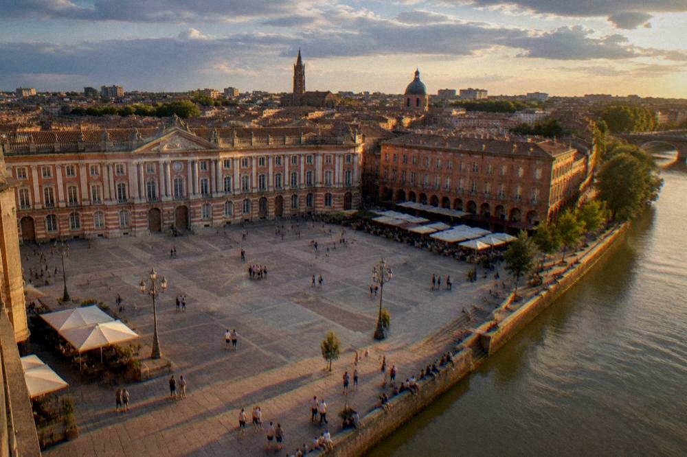 People sitting on the Garonne riverbank at sunset with the Toulouse skyline behind them