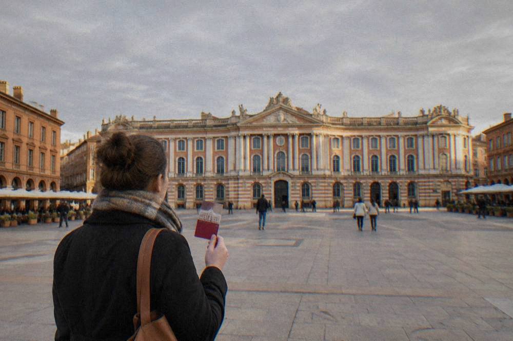 A visitor holding a city pass in front of the Capitole building in Toulouse