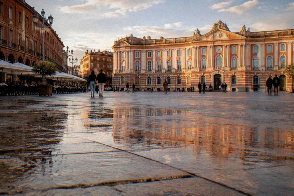 A wide Toulouse square with a grand pink brick facade in late golden light