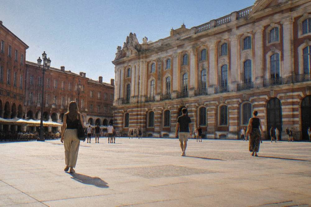 Visitors walking past pink brick buildings in the historic center of Toulouse