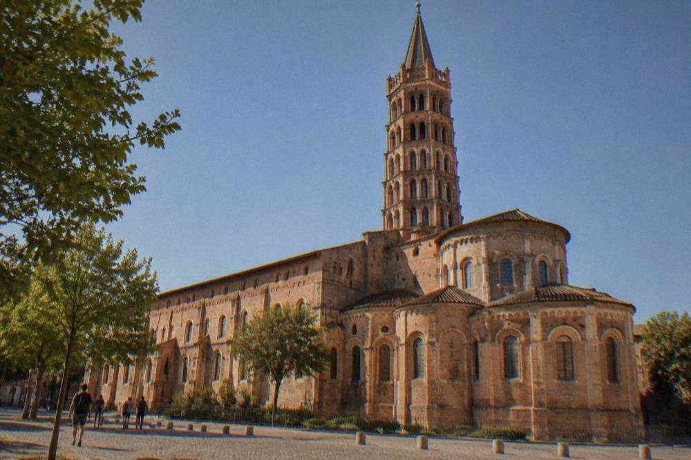 The tower and brick facade of the Saint-Sernin basilica in Toulouse under a clear sky