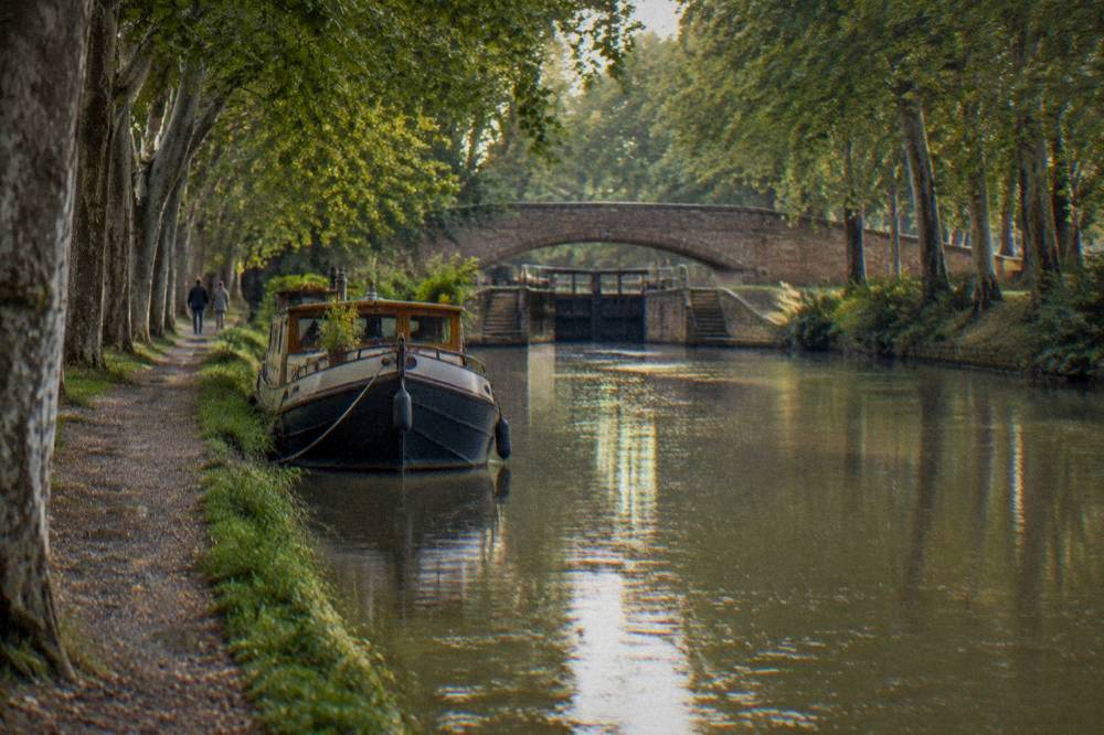 A canal boat moored on the tree lined banks of the Canal du Midi