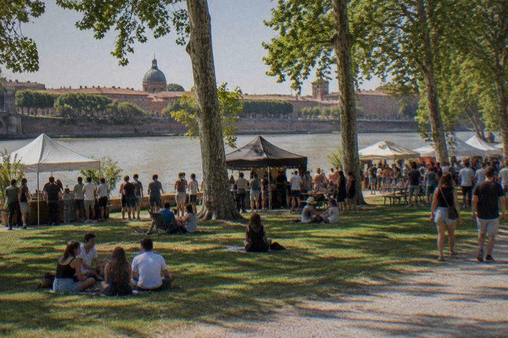 An outdoor food festival with stalls and crowds along a riverside lawn