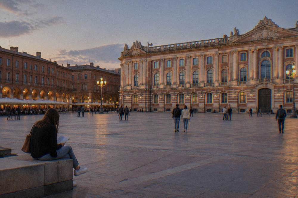 Visitors reading a museum entrance sign on a wide pink brick sidewalk in Toulouse