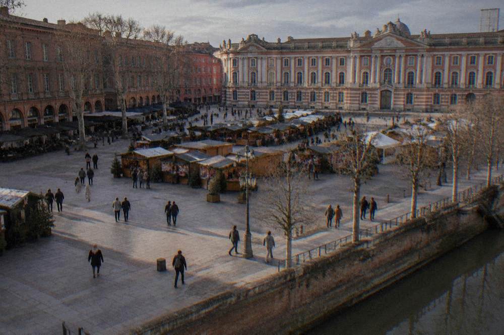 A Christmas market with wooden chalet stalls in front of a grand pink-brick city square