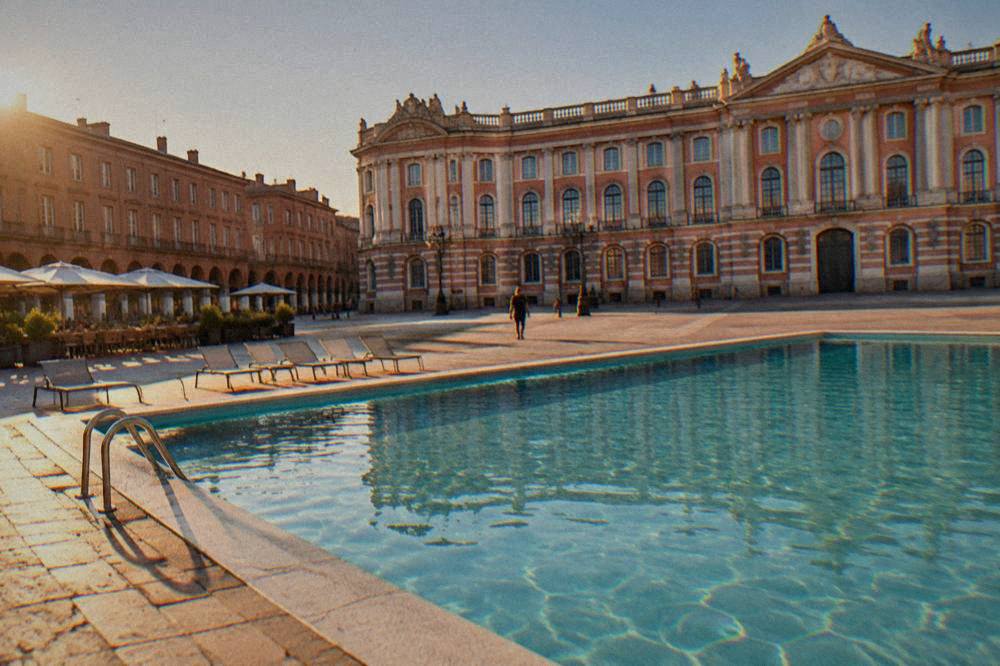 Sunlit outdoor swimming pool with clear blue water and empty loungers in a French city