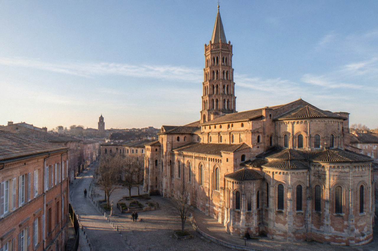 Pink brick buildings along a Toulouse street with the Basilique Saint-Sernin tower rising in the distance
