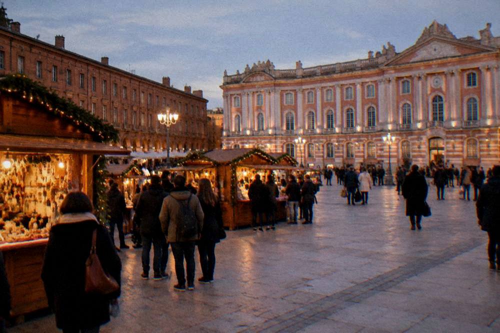 A crowd browsing wooden chalet stalls at an outdoor market in central Toulouse