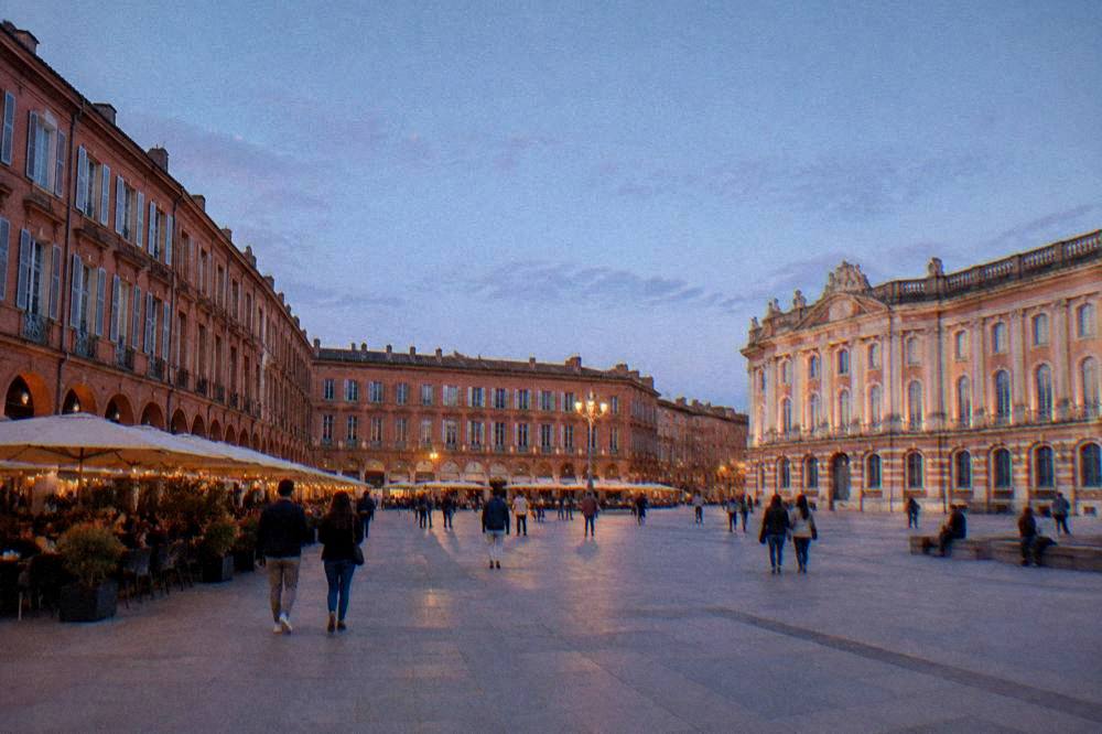A pink-brick street in central Toulouse with shutters and a cafe terrace in the evening