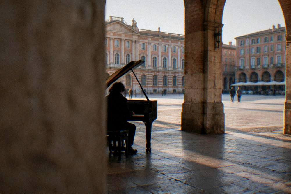 A piano on a stone cloister floor under medieval arches