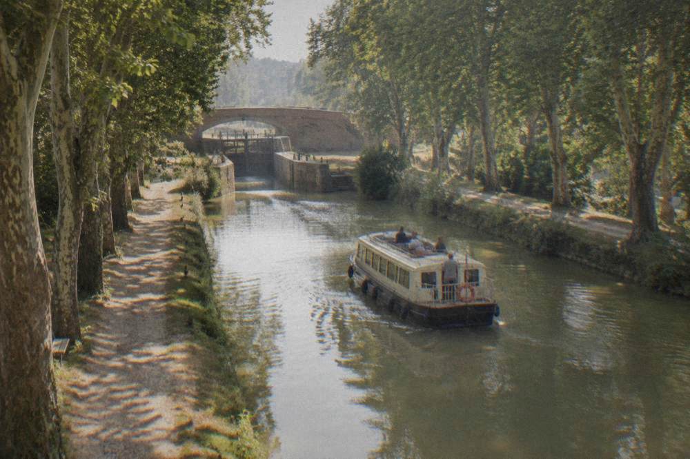 A canal boat moving slowly along the tree lined Canal du Midi