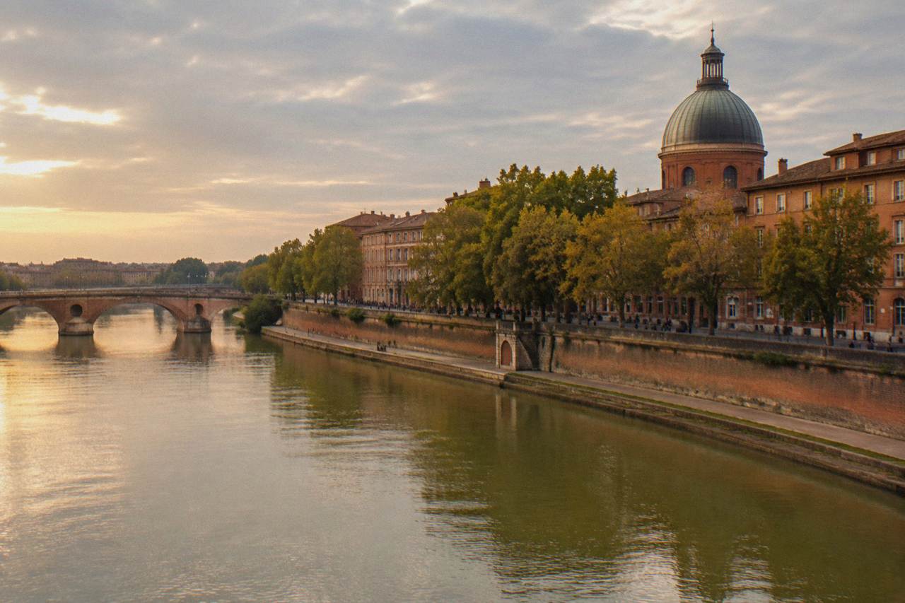Pink brick buildings along a Toulouse street with the dome of the Hospitaller structure in the background
