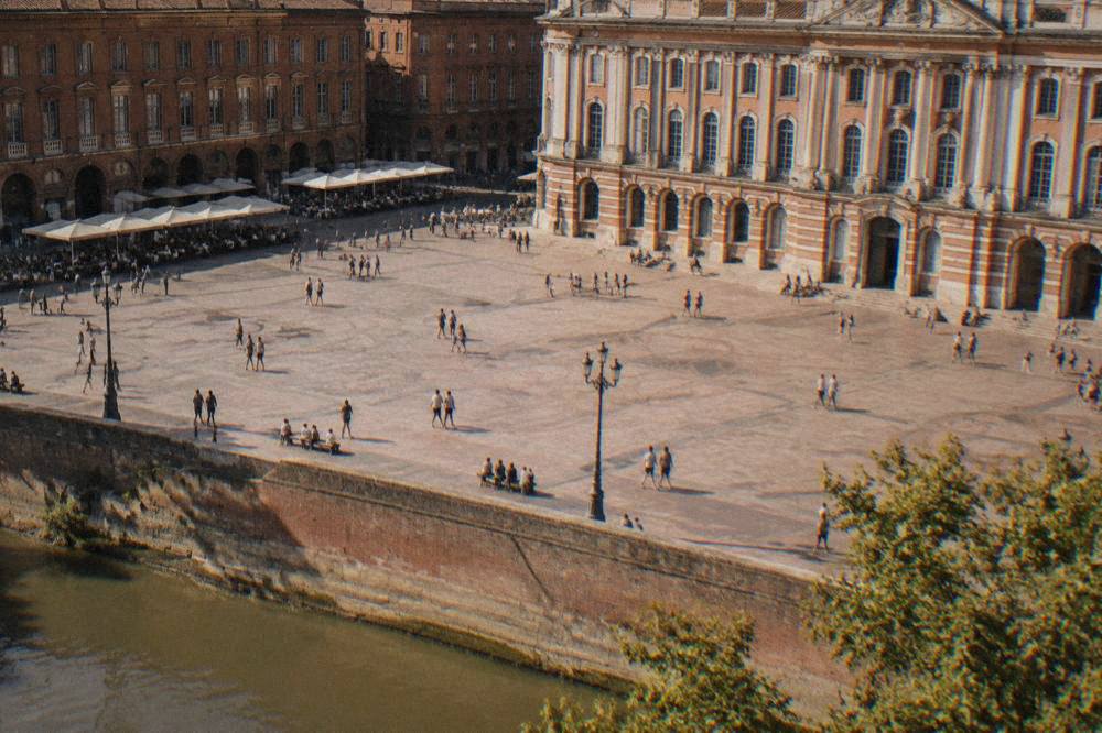 Sunlit square in Toulouse with cafe tables and pink brick facades