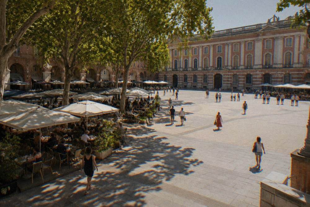 A shaded Toulouse square with cafe tables and plane trees during a hot summer afternoon