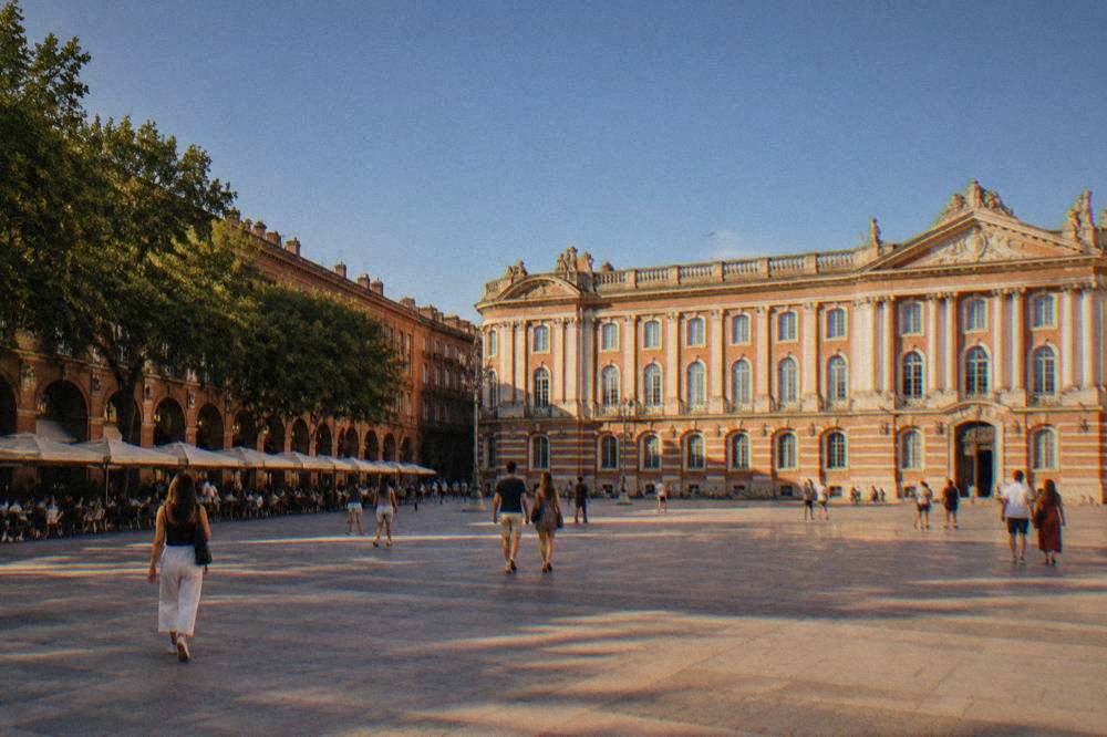 A sunny June day on a Toulouse plaza with the pink city walls glowing in warm light