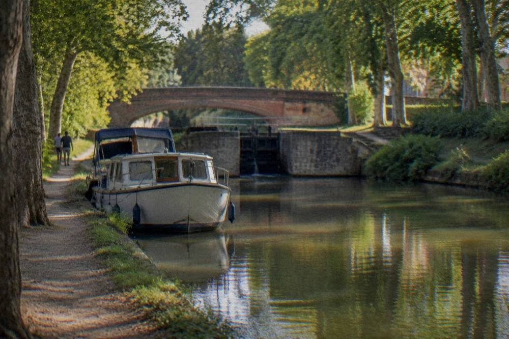 A small boat moored on the Canal du Midi under a warm afternoon sun in Toulouse
