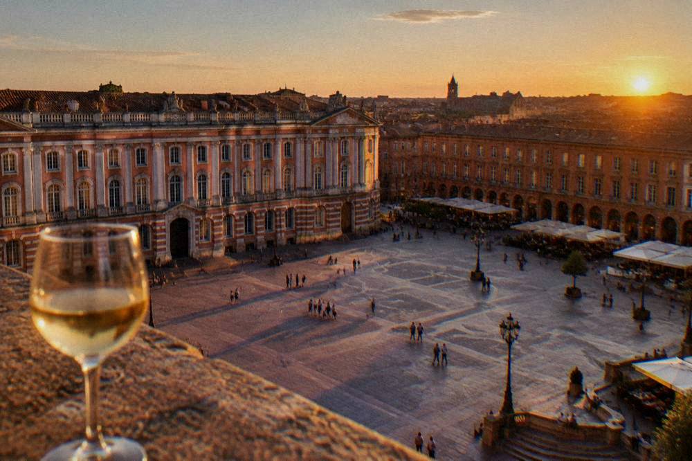 A sunset over Toulouse rooftops with a wine glass in the foreground
