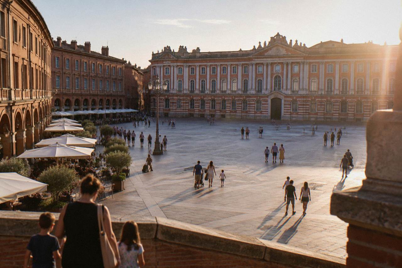 Families walking past pink brick buildings on a sunny day in Toulouse
