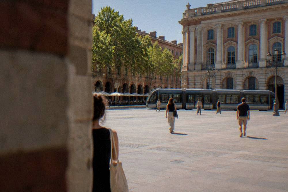 A modern tram traveling along a Toulouse street lined with trees