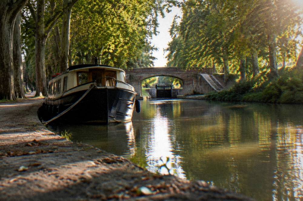 A canal boat moored on the Canal du Midi with plane trees overhanging the water