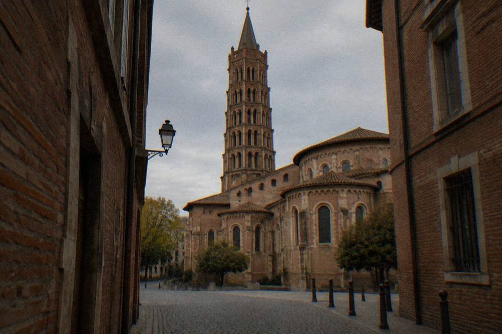The red brick Basilique Saint-Sernin tower seen from a narrow street in Toulouse