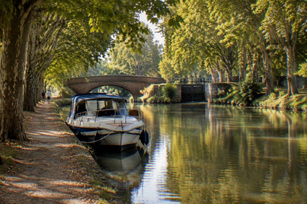 A tree-lined canal with a pleasure boat moored beside the towpath