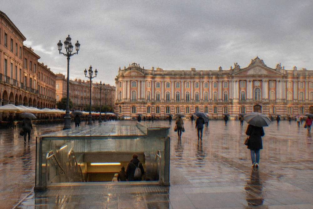 A covered metro station entrance in Toulouse with wet pavement and people with umbrellas