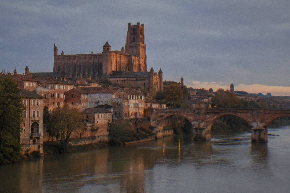 A stone bridge and riverside buildings in Albi seen under a grey sky