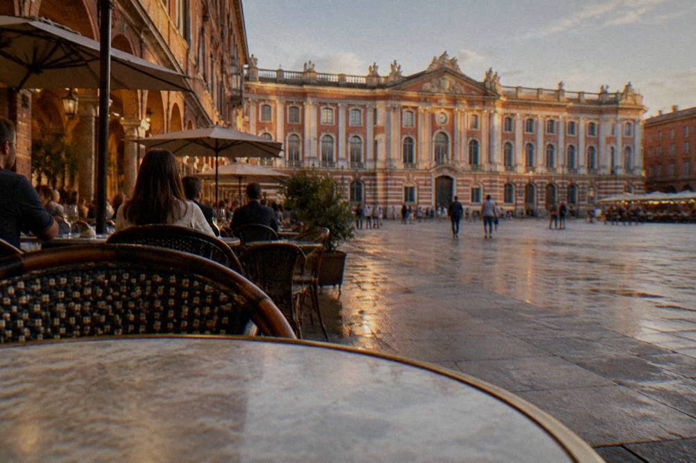 People seated at outdoor tables on a lit brick street in Toulouse in the evening